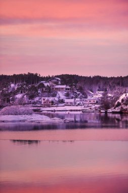 Gün batımının güzel portakal rengi günbatımı manzarası. Norveç 'in Tonsberg şehrinin yakınlarındaki fiyortta pembe bulutların yansıması. Karlı evlerde kırağı var.