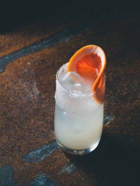 Beyaz roily kokteyl pürüzsüz bir şeffaf cam buz küpleri ile arkadaki paslı bir arka plan üzerinde taze greyfurt parçası ile dekore edilmiştir. Moody ışık, dikey yönlendirmesi, metin alanı