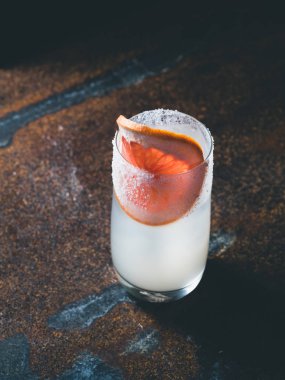 Pürüzsüz bir şeffaf cam buz küpleri ile beyaz roily kokteyl paslı bir arka plan üzerinde önünde taze greyfurt parçası ile dekore edilmiştir. Moody ışık, dikey yönlendirme