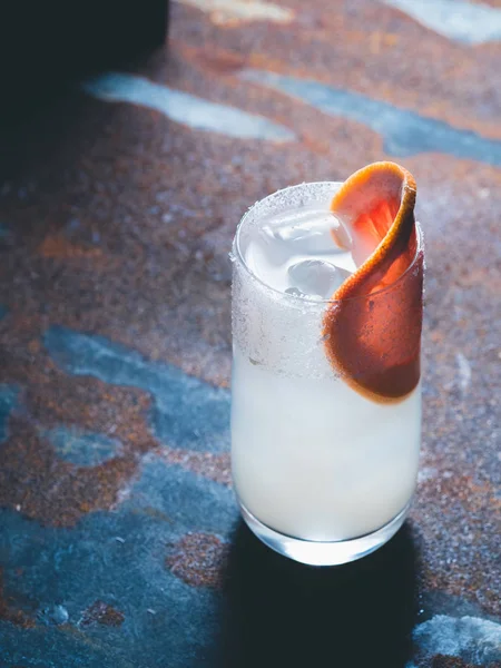 Cocktail bianco di giglio con cubetti di ghiaccio in vetro trasparente liscio decorato con pompelmo fresco a destra su fondo arrugginito. Retroilluminazione, orientamento verticale, spazio di testo — Foto Stock
