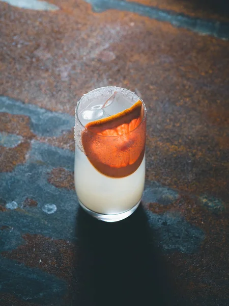 Vit roily cocktail med isbitar i en smidig genomskinligt glas inredda med bit färsk grapefrukt till höger på en rostig bakgrund. Bakgrundsbelysning, lodrät orientering, — Stockfoto