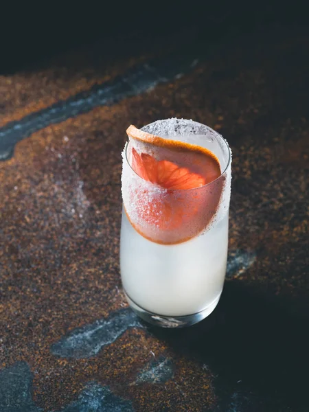 Pürüzsüz bir şeffaf cam buz küpleri ile beyaz roily kokteyl paslı bir arka plan üzerinde önünde taze greyfurt parçası ile dekore edilmiştir. Moody ışık, dikey yönlendirme
