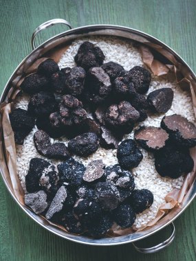 Birçok siyah trüf mantar yarısı, kesilmiş bazı domalan metalik bir tencerede bütün bazılarıdır. Turkuaz ahşap arka plan, dikey yönlendirme