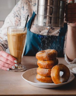 Pishki - Rus çörek. Kız toz pudra şekeri çörek üzerinde geleneksel kantinde bir arka plan üzerinde uzun bir şeffaf bardak kakao içmeye kız. Dikey fotoğraf