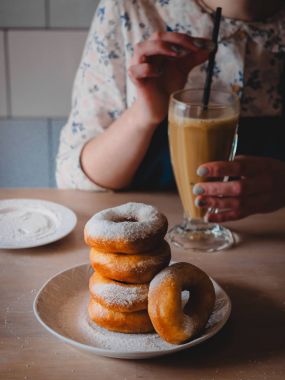 Pishki - Rus yağda kızartılmış çörekler ile pudra şekeri, kakao geleneksel kantinde bir arka plan üzerinde uzun bir şeffaf bardak içme kız silkeledi. Dikey fotoğraf