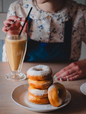 Pishki - Rus yağda kızartılmış çörekler ile pudra şekeri, kakao geleneksel kantinde bir arka plan üzerinde uzun bir şeffaf bardak içme kız silkeledi. Dikey fotoğraf