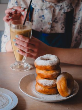 Pishki - Rus yağda kızartılmış çörekler ile pudra şekeri, kakao geleneksel kantinde bir arka plan üzerinde uzun bir şeffaf bardak içme kız silkeledi. Dikey fotoğraf