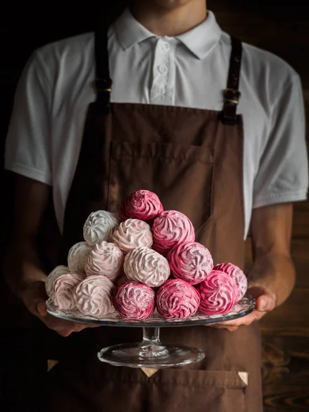 Bellissimo Zefir rosa (Zephyr, zephir) - dolciumi simili a marshmallow - su un piatto trasparente su mani di panettieri — Foto Stock