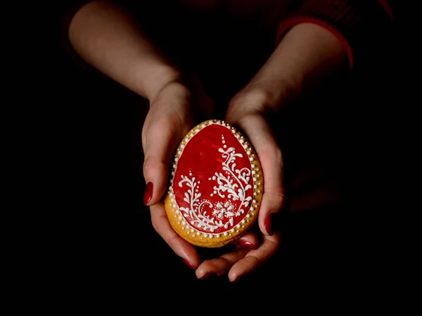 Easter egg-shaped cookies. Female hands holding a cookie. horizontal photo, dark background