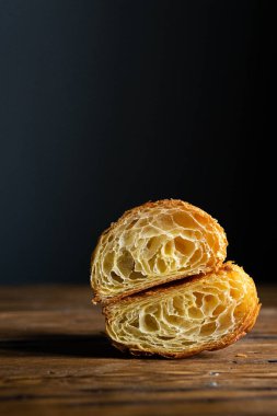 Mükemmel kruvasan kesimi. Ahşap bir masada sade kruvasan kesiği, siyah arka plan.