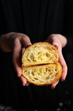 Mükemmel kruvasan kesimi. Düz kruvasan, siyah arka planda bir kadının ellerinde kesilmiş.