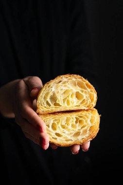 Mükemmel kruvasan kesimi. Düz kruvasan, siyah arka planda bir kadının ellerinde kesilmiş.