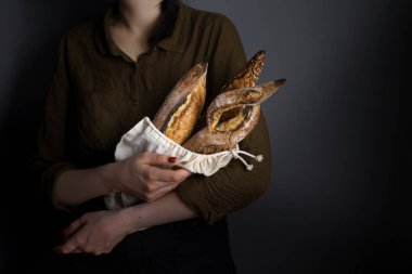 Ekmek torbasında Fransız ekmeği, kadın fırıncı, baget ve bitki karışımı, yatay fotoğraf.