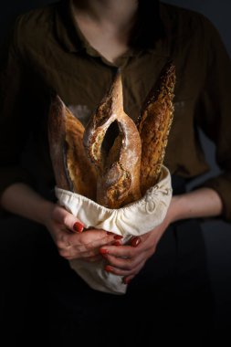 Ekmek çantasındaki Fransız ekmeği kadın fırıncı, baget ve bitki karışımı, dikey fotoğraf.