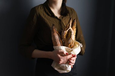 Ekmek torbasında Fransız ekmeği, kadın fırıncı, baget ve bitki karışımı, yatay fotoğraf.