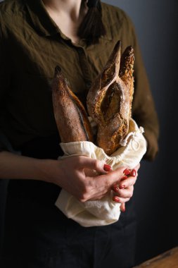 Ekmek torbasında Fransız ekmeği, kadın fırıncı, baget ve bitkisel fougasse. dikey resim