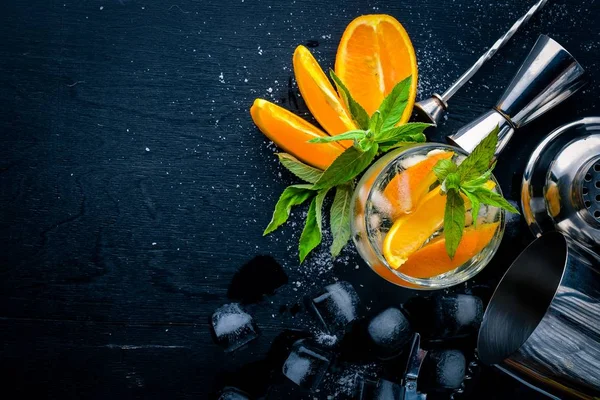 Cocktail of oranges and menthol with ice, on a black wooden surface. Top view. Free space. — Stock Photo, Image