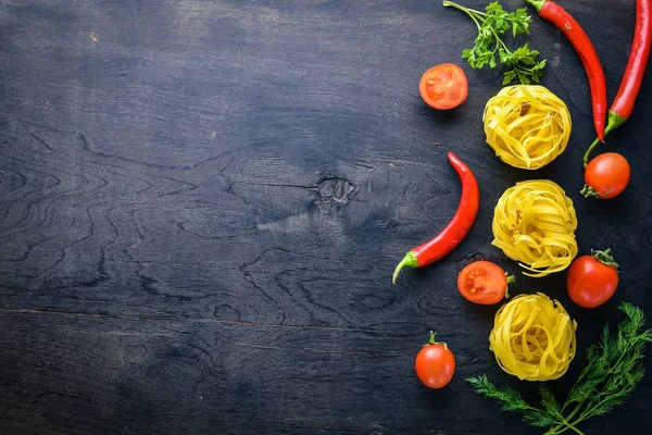 Pasta dengan sayuran, tomat ceri, cabai dan bawang putih. Pada latar belakang kayu. Ruang kosong untuk teks. Tampilan atas — Stok Foto