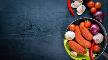 Taze sebze ile bir tavada ızgara sosis. Siyah yüzeyi ahşap. Üstten Görünüm.