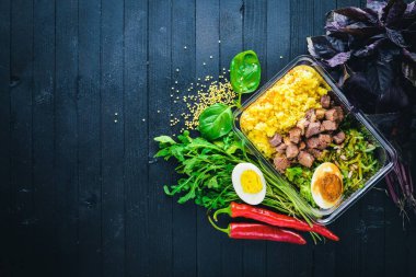 Et ve taze sebze ile haşlanmış yulaf lapası. Sağlıklı bir diyet yemek. Öğle Yemeği boks. Siyah ahşap arka plan üzerinde. Üstten Görünüm. Metin için boş alan.