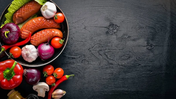 Taze sebze ile bir tavada ızgara sosis. Siyah yüzeyi ahşap. Üstten Görünüm.