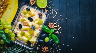 Porridges yoğurt, ananas, üzüm ve karpuz. Sağlıklı bir diyet yemek. Öğle Yemeği boks. Siyah ahşap arka plan üzerinde. Üstten Görünüm. Metin için boş alan.