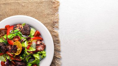 Salata taze salatalık, domates ve yeşillik bir plaka ahşap tahta üzerinde ızgara et ile. Üstten Görünüm. Boş alan.