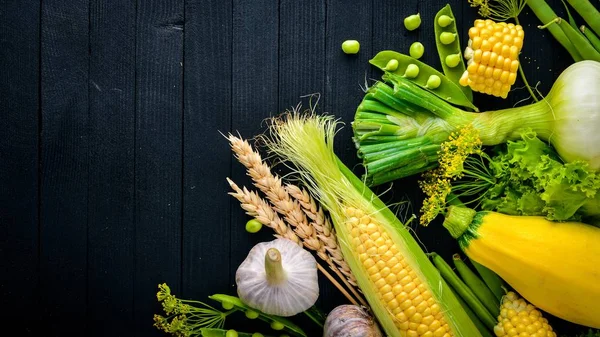 Çok çeşitli ham taze sebze. Mısır, kabak, marul, yeşillik. Siyah ahşap arka plan üzerinde. Üstten Görünüm. Metniniz için boş alan.