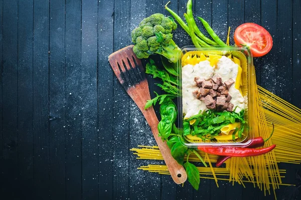 Et ve taze sebze ile makarna. Sağlıklı bir diyet yemek. Öğle Yemeği boks. Siyah ahşap arka plan üzerinde. Üstten Görünüm. Metin için boş alan.