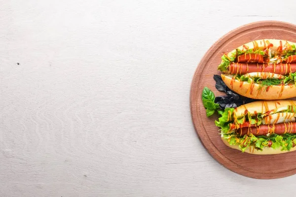 Perro caliente con salchicha a la parrilla, mostaza y ketchup, cebollas y verduras sobre fondo de madera. Vista superior. Espacio libre . — Foto de Stock