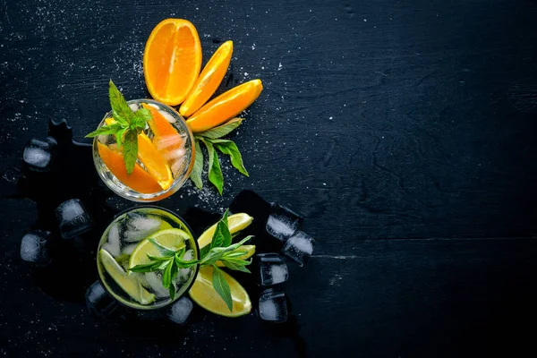 Refreshing cocktails of citrus fruit and menthol with ice, on a black wooden surface. Top view. Free space. — Stock Photo, Image