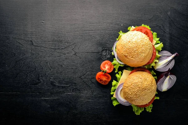 Hamburguesa con queso, carne, tomates y cebollas y hierbas. Sobre fondo de madera. Vista superior. Espacio libre . — Foto de Stock