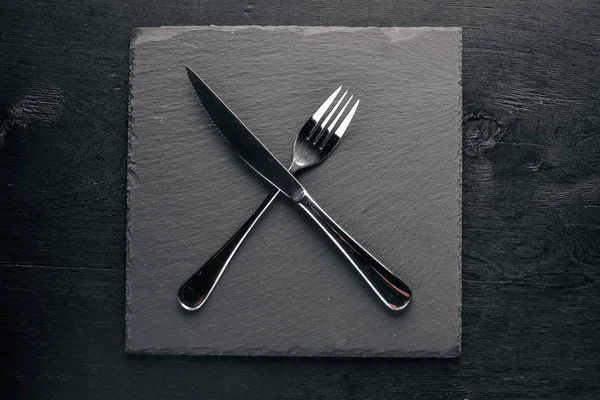 Μαύρος πίνακας πετρών με τα μαχαιροπήρουνα. Σε ένα ξύλινο υπόβαθρο. Κορυφαία επισκόπηση. Ελεύθερου χώρου. — Φωτογραφία Αρχείου