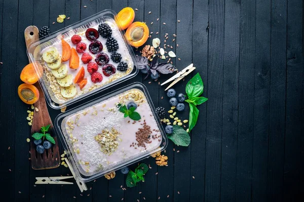 Haferflocken mit Joghurt und Früchten. gesunde Ernährung. Lunchboxen. auf schwarzem Holzgrund. Ansicht von oben. Freiraum für Text. — Stockfoto