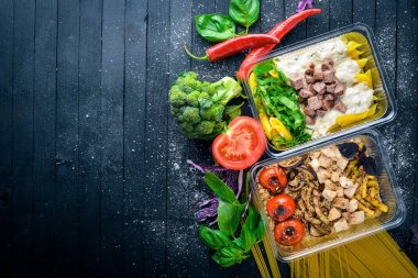 Makarna ve buğday eti ve taze sebze ile. Sağlıklı bir diyet yemek. Öğle Yemeği boks. Siyah ahşap arka plan üzerinde. Üstten Görünüm. Metin için boş alan.