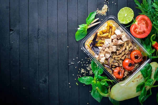 Risotto pirinci et ve ızgara sebzeler ile. Sağlıklı bir diyet yemek. Öğle Yemeği boks. Siyah ahşap arka plan üzerinde. Üstten Görünüm. Metin için boş alan.