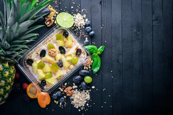 Porridges yoğurt, ananas, üzüm ve karpuz. Sağlıklı bir diyet yemek. Öğle Yemeği boks. Siyah ahşap arka plan üzerinde. Üstten Görünüm. Metin için boş alan.