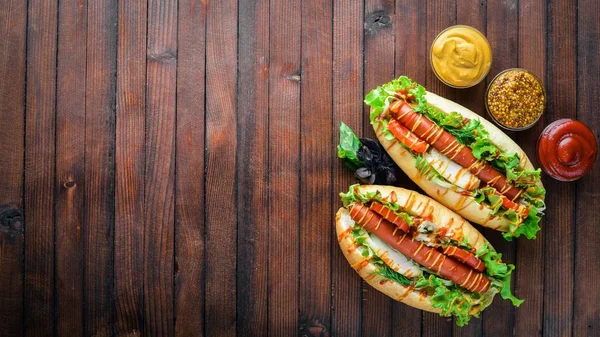 Sosis ızgara sosis, hardal ve ketçap, soğan ve Yeşiller ahşap arka plan üzerinde. Üstten Görünüm. Boş alan.