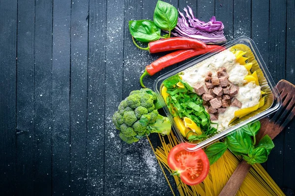 Et ve taze sebze ile makarna. Sağlıklı bir diyet yemek. Öğle Yemeği boks. Siyah ahşap arka plan üzerinde. Üstten Görünüm. Metin için boş alan.