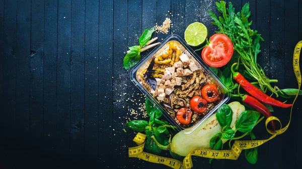 Risotto pirinci et ve ızgara sebzeler ile. Sağlıklı bir diyet yemek. Öğle Yemeği boks. Siyah ahşap arka plan üzerinde. Üstten Görünüm. Metin için boş alan.