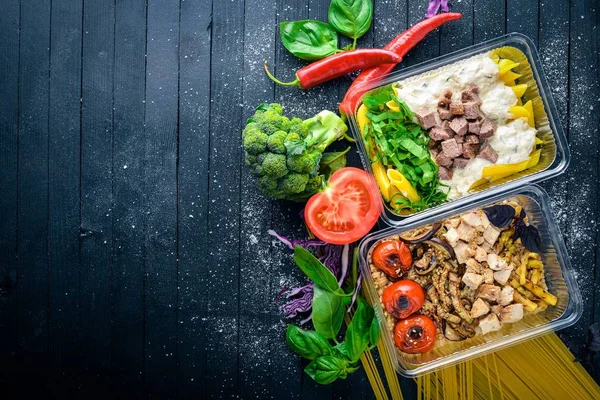 Makarna ve buğday eti ve taze sebze ile. Sağlıklı bir diyet yemek. Öğle Yemeği boks. Siyah ahşap arka plan üzerinde. Üstten Görünüm. Metin için boş alan.