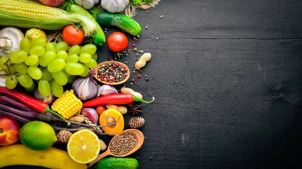 Çiğ sebze, meyve ve baharat bir siyah ahşap yüzey üzerinde büyük bir seçim. Metniniz için boş alan. Üstten Görünüm.