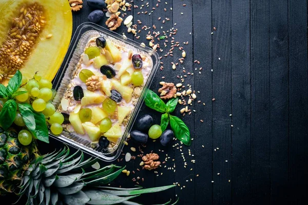 Porridges yoğurt, ananas, üzüm ve karpuz. Sağlıklı bir diyet yemek. Öğle Yemeği boks. Siyah ahşap arka plan üzerinde. Üstten Görünüm. Metin için boş alan.