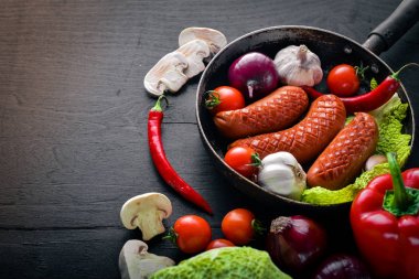 Taze sebze ile bir tavada ızgara sosis. Siyah yüzeyi ahşap. Üstten Görünüm.