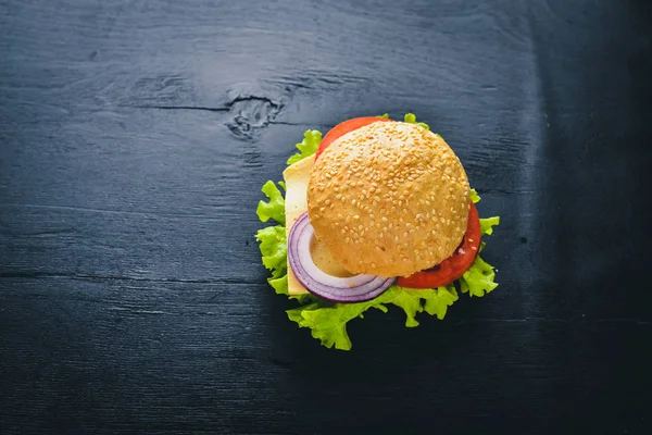 Hamburguesa con queso, carne, tomates y cebollas y hierbas. Sobre fondo de madera. Vista superior. Espacio libre . — Foto de Stock