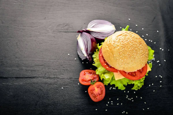 Hambúrguer com queijo, carne, tomate e cebola e ervas. Sobre fundo de madeira. Vista superior. Espaço livre . — Fotografia de Stock