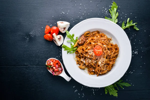 Kiraz domates, zeytin ve parmesan peyniri ile mantarlı makarna. İtalyan yemeği. Bir siyah ahşap yüzeye. Metniniz için boş alan. Üstten Görünüm.