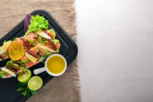 Somon Bruschetta otlar ve parmesan peyniri ekmeğin. Soğuk aperatifler. İtalyan mutfağı. Ahşap arka plan üzerinde.