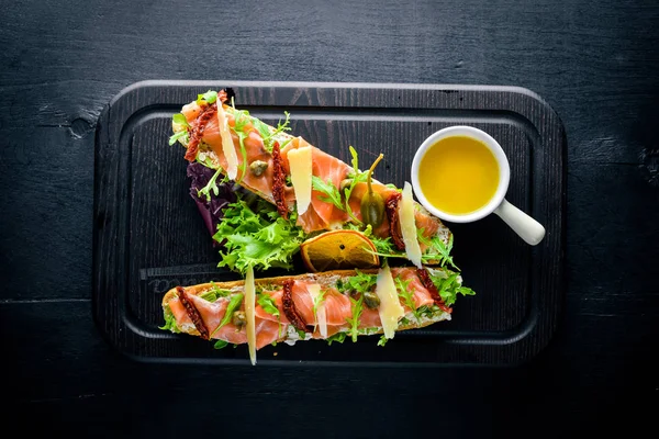 Somon Bruschetta otlar ve parmesan peyniri ekmeğin. Soğuk aperatifler. İtalyan mutfağı. Ahşap arka plan üzerinde.