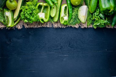 Yeşil sebzeler büyük bir set keten kumaş, ahşap zemin üzerinde ortaya koydu. Üstten Görünüm. Boş alan.